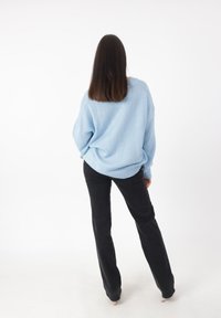 Hellblaues, übergroßes Strickoberteil mit geripptem Saum, kombiniert mit schwarzen, ausgestellten Hosen. Der Stoff wirkt weich mit einer strukturierten Oberfläche.