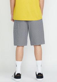 Striped gray shorts with an elastic waistband and side pockets, paired with a yellow shirt and black sneakers, coupled with white socks.