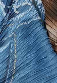 Faltenstoff in Blau- und Brauntönen mit einer strukturierten Oberfläche. Der blaue Abschnitt weist ein wirbelndes Muster und einen dezenten Glanz auf.
