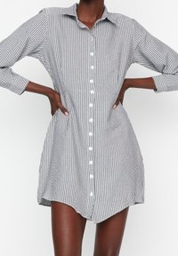 Robe chemise avec des rayures verticales noires et blanches, un col, des manches longues et un ourlet légèrement courbé. Fabriquée dans un tissu léger.