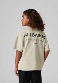 Heleda roheline puuvillane t-särk lühikeste varrukatega, mille seljal on must tekst "ALLSAINTS" ja jaapani kirjaviis. Mugav lõige.