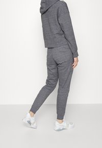 Šedá krátká mikina s manžetami a šedé tepláky se stejným odstínem. Model nosí bílé sportovní boty se světlými doplňky.