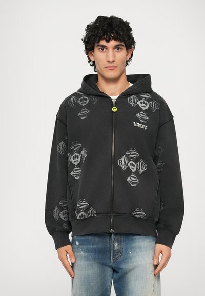 Felpa nera con zip e motivi grafici grigi, con teschi e elementi incrociati. Include tasche frontali e cappuccio con coulisse.