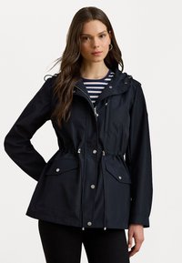 Námořnická modrá雨jacket s utaženým pasem, zipem vpředu, nastavitelnou kapucí a dvěma předními kapsami. Lehká tkanina s hladkým povrchem.