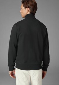 Svart sweatshirt med hög hals, ribbade ärmslut och nederkant. Har en jämn textur och en enkel, minimalistisk design. Bakvy.