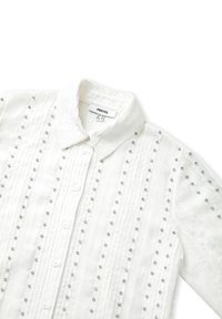 Witte shirt met kraag, voorzien van verticale plooien en duidelijke edelsteentjes die gelijkmatig over de stof zijn verdeeld. Knopsluiting aan de voorkant.