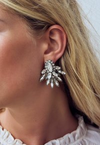 Clear, teardrop-shaped earrings with multiple sparkling, clear gemstones on a silver-tone backing, featuring a layered, floral-inspired design.
