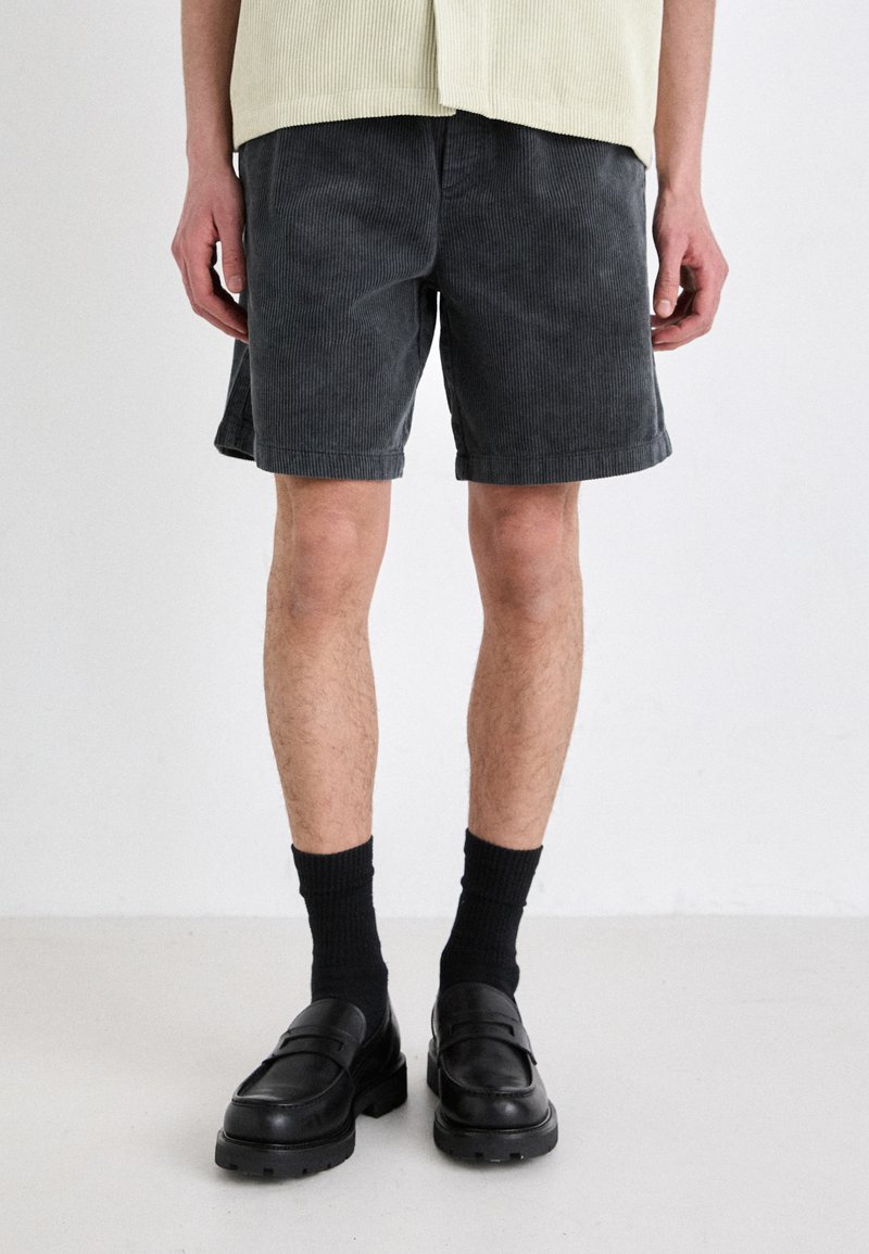 Gray corduroy shorts with a textured finish, featuring a relaxed fit and rolled hems, paired with black loafers and crew socks.