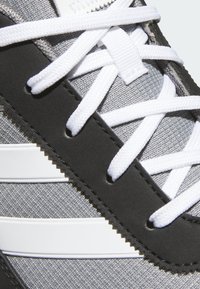 Szary tekstylny wierzch z czarnymi akcentami z tworzywa sztucznego. Białe sznurowadła i trzy białe paski po boku. Teksturowana powierzchnia.