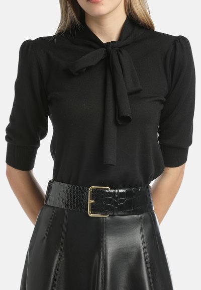 Czarny dzianinowy top z wiązanym dekoltem, krótkimi bufiastymi rękawami, połączony z czarną spódnicą z ekologicznej skóry i teksturowanym czarnym paskiem z złotą klamrą.