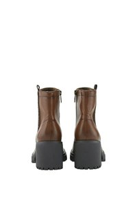 Botas de cuero marrón hasta el tobillo con tacones de bloque, que presentan un cierre lateral y acentos texturizados en los lados. Suelas gruesas de goma gris.