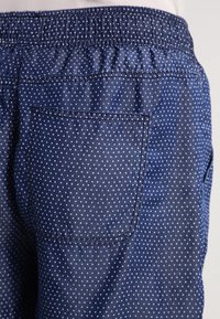 Siniset, kevyet kangashousut, joissa on sinisiä pilkkuja, joustava vyötärö ja yksi takatasku. Sileä pinta.