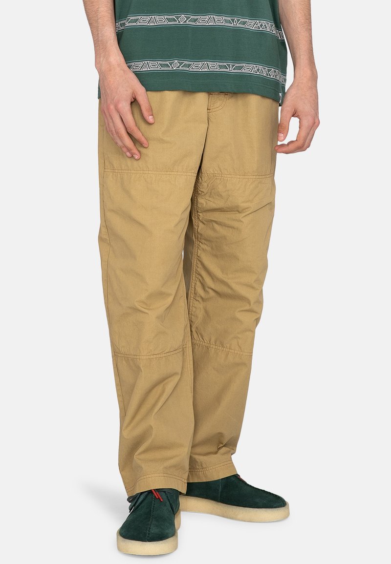 Pantalons cargo beige en tissu léger, avec plusieurs poches, une coupe décontractée et des détails de couture visibles.