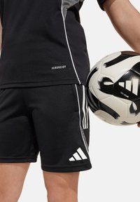 Shorts deportivos negros con rayas blancas y un logo de Adidas, acompañados de un balón de fútbol en blanco y negro, que presenta patrones geométricos en contraste.