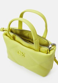 Žlutá kožená kabelka s krátkými uchy, opatřená zipovým zapínáním a prošívaným designem. Uvnitř je na jemné podšívce vyražena značka.