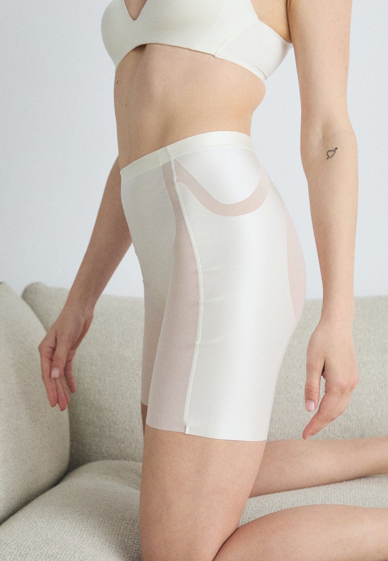 High-waisted, cream-colored shaping shorts made of smooth, sheer fabric with subtle curve design details along the sides.