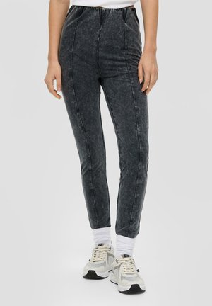 Jogging en denim noir avec taille élastique, design ajusté, coutures latérales et texture délavée. Associé à des sneakers sportives et des chaussettes blanches.