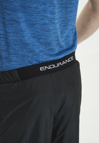 Blått melerat träningslinne möter svarta shorts med elastisk midja som har "ENDURANCE" i vitt. Slät textur, figursydd design.