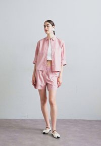 Short-sleeved, pink striped button-up shirt paired with matching shorts, featuring an elastic waistband, worn with white slip-on shoes.