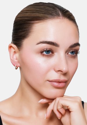 Boucle d'oreille en or avec une petite rangée de cristaux clairs, texture lisse et forme circulaire, portée par un mannequin au maquillage neutre et à la peau claire.