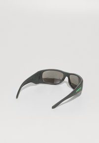 Gafas de sol de plástico gris con lentes oscuros, con un atrevido logo verde en el lateral. Diseño elegante con brazos curvados.