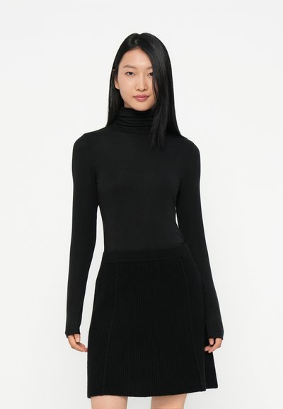 Top negro de cuello alto con mangas largas combinado con una falda de punto acanalado negra. Ambas prendas presentan una forma ajustada con una textura suave.