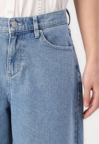 Lyse blå denimjeans med høy midje, utstyrt med metallknappelukking, frontlommer og subtile sømdetaljer.