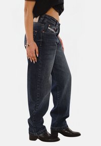 High-waisted, dark blue denim jeans with a relaxed fit, featuring front and back pockets, orange stitching, and a leather label at the back waistband.
