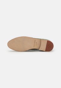 Suola di scarpa con una base in pelle beige, caratterizzata da una finitura liscia e un logo in rilievo a forma di scudo. Il tallone presenta un accentuato tono marrone-rossastro.