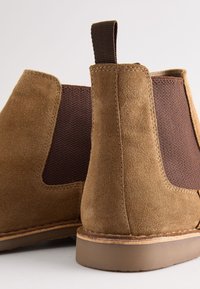 Bruine suède enkellaarsjes met elastische zijpanelen, rubberen zolen en een achteraan bevestigde lus voor gemakkelijk aan- en uittrekken. Textielaccent met structuur aan de zijkanten.