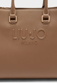 Braune Kunstleder-Handtasche mit glänzend geprägtem "LIU·JO MILANO"-Logo, zwei Griffen und strukturierter Oberfläche. Dezente Nähte und goldfarbene Hardware-Details.
