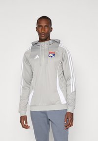 Grå hættetrøje med hvid stribet design, med Olympique Lyonnais-logoet på brystet og en justerbar snøre i hætten.