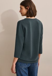Suéter de color azul oscuro con mangas tres cuartos, con un escote redondo y textura suave, combinado con pantalones de mezclilla.