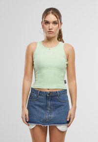 Mintgrön ribbad linne med rund hals och logodetalj, kombinerat med en högmidjad denimminikjol med fransade kanter.