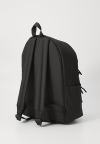 Sac à dos en tissu noir avec des sangles rembourrées, un haut arrondi, des poches latérales et des boucles réglables pour un maintien sécurisé. Présente une surface texturée.