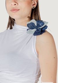 Top bianco senza maniche con un design arricciato e una grande decorazione floreale blu con petali testurizzati e paillettes sulla spalla.