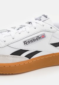 Reebok sneaker with white leather upper, black accents, suede toe cap, and gum rubber sole. Features white laces and branded tag.