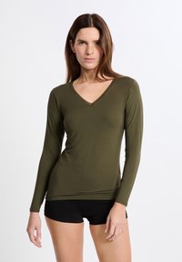 Maglietta a maniche lunghe verde oliva con scollatura a V, caratterizzata da un bordo texture. Tessuto morbido e elasticizzato, vestibilità slim. Il modello indossa pantaloni corti neri.