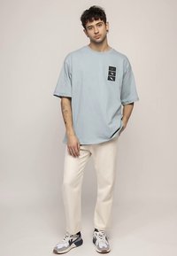 Lichtblauw oversized T-shirt met een boxlogo op de borst, gecombineerd met off-white rechte broekspijpen en sneakers in meerdere kleuren.