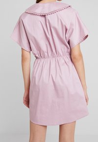 Abito in cotone rosa con maniche corte, vita elastica e collo a scallop. Texture liscia e orlo fino al ginocchio.