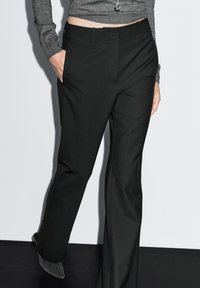 Black tailored trousers with a smooth texture, flat front, and side pockets, paired with a fitted gray long-sleeve top.