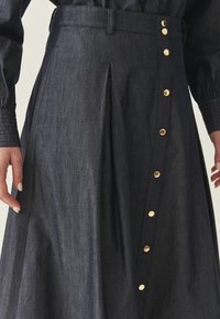 Spódnica dżinsowa w ciemnym odcieniu z plisowanym wzorem, z złotymi guzikami po bokach i gładką fakturą.