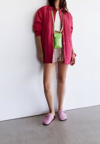 Chemise rose surdimensionnée à boutons, débardeur blanc court, short rayé, sac bandoulière vert néon et sabots roses avec semelles foncées.