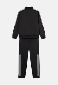 Survêtement noir en tissu lisse. Veste zippée avec col haut, manches longues et bandes blanches sur les épaules. Pantalons avec taille élastique.