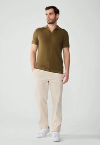 Olivgrünes, geripptes Polohemd mit weicher Textur, getragen mit hellbeigen Hosen und weißen Sneakers. Hat einen klassischen Kragen und kurze Ärmel.