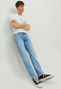 Jeans rectos de color azul claro con un acabado desteñido, combinados con una camiseta blanca sencilla. Zapatillas negras con acentos blancos y textura de lona.