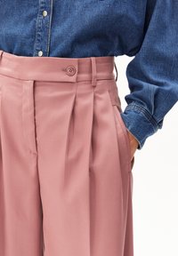 Roze op maat gemaakte broek met plooien, zijzakken en een knoopsluiting, gecombineerd met een blauwe spijkerblouse met een knoopkraag.