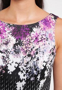 Ärmelloses Kleid mit Blumenmuster und runder Ausschnitt. Mit lila, rosa und weißen Blumen auf schwarzem Hintergrund und einer strukturierten Musterung.