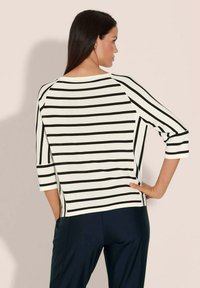 Gestreepte gebreide top in wit en zwart, met driekwartraglanmouwen, een brede halslijn en zijsplitten aan de onderrand.