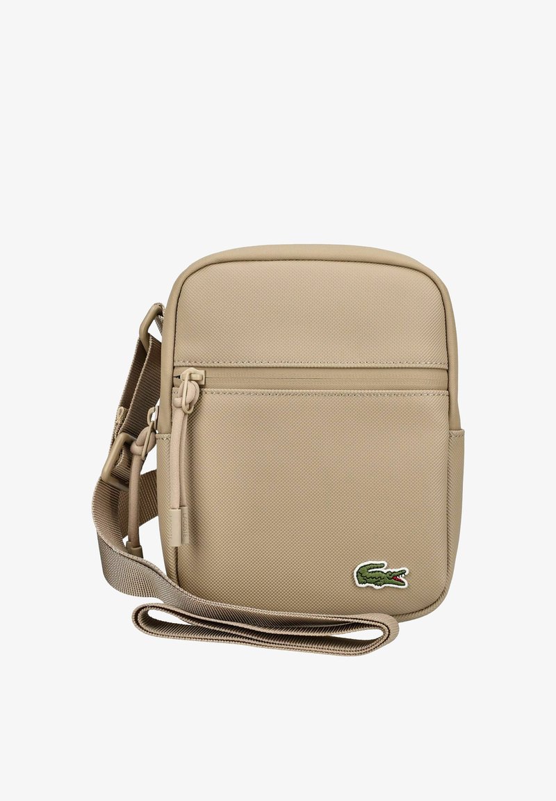 Sac bandoulière beige avec poche zippée à l'avant, sangle réglable et petit logo crocodile vert dans le coin inférieur droit.
